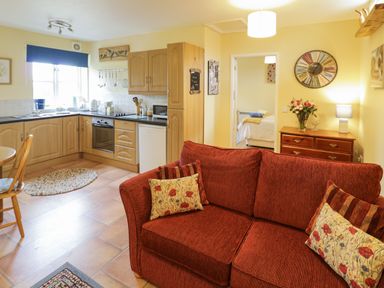 A kitchen and living area with wooden cabinets a red sofa and a wooden dresser at The Garden Lodge in Upton Cressett near Bridgnorth