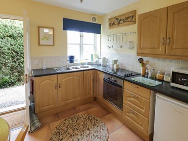 A kitchen with wooden cabinets a circular rug utensils and appliances at The Garden Lodge in Upton Cressett near Bridgnorth