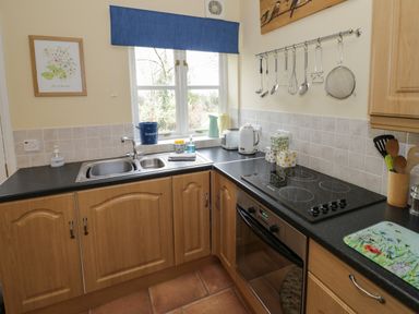 A kitchen with wooden cabinets a black countertop a stovetop an oven a sink and various utensils at The Garden Lodge in Upton Cressett near Bridgnorth