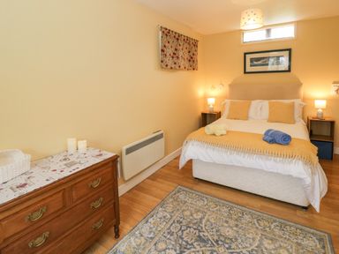 A bedroom with a bed, bedside tables, a wooden dresser, and a patterned rug at The Garden Lodge in Upton Cressett near Bridgnorth