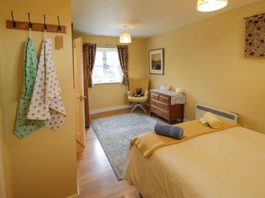 A bedroom with a bed towels armchair chest of drawers and a window at The Garden Lodge in Upton Cressett near Bridgnorth