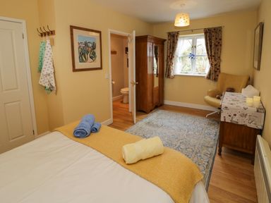 A bedroom with a bed covered in towels a wooden wardrobe a chair a window with curtains and a side table at The Garden Lodge in Upton Cressett near Bridgnorth