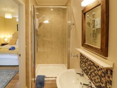 A bathroom with a shower cubicle sink and mirror next to a bedroom at The Garden Lodge in Upton Cressett near Bridgnorth