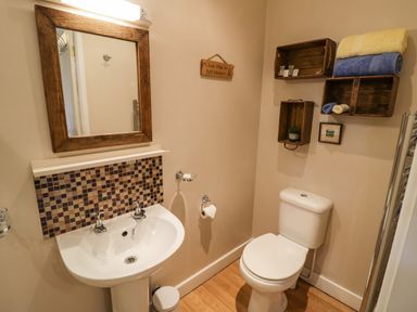 A bathroom with a sink a mirror and a toilet with towels on shelves on the wall at The Garden Lodge in Upton Cressett near Bridgnorth