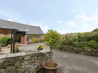 A stone wall with potted plants and a building with slate roof and wooden door at Pentre Barn in Llantilio Pertholey near Mardy