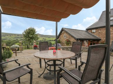 An outdoor patio with a round table and chairs under an awning overlooking a garden and hills at Pentre Barn in Llantilio Pertholey near Mardy