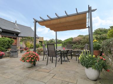 An outdoor patio with a table and chairs under a pergola surrounded by potted plants at Pentre Barn in Llantilio Pertholey near Mardy