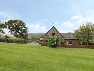 A stone house with a balcony and green lawn surrounded by trees at Pentre Barn in Llantilio Pertholey near Mardy
