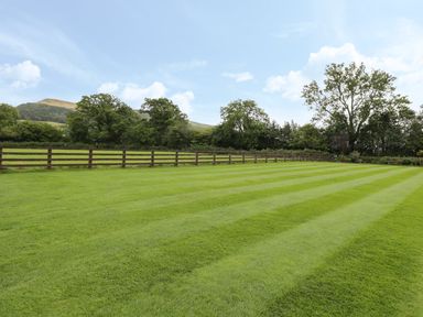 A large lawn with striped mowing patterns and a wooden fence with trees in the background at Pentre Barn in Llantilio Pertholey near Mardy