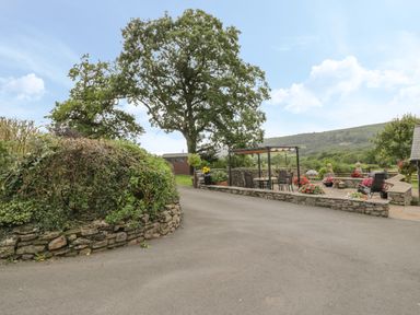 An outdoor patio area with chairs tables and flowers near trees and a stone wall at Pentre Barn in Llantilio Pertholey near Mardy