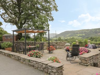 Outdoor patio area with table, chairs, flowers, and a pergola with a landscape view at Pentre Barn in Llantilio Pertholey near Mardy