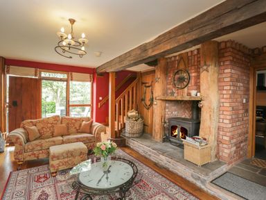 A living room with a sofa ottoman glass coffee table rug fireplace and wooden beams at Pentre Barn in Llantilio Pertholey near Mardy