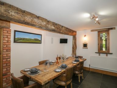 A dining room with a wooden table set for six and leather chairs at Pentre Barn in Llantilio Pertholey near Mardy