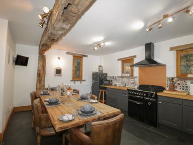A kitchen with a wooden dining table set with dishes and glasses and dark cabinets at Pentre Barn Llantilio Pertholey near Mardy
