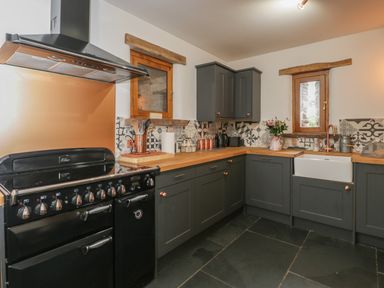 A kitchen with dark grey cabinets wooden countertops a black stove and a patterned tile backsplash with two small wooden windows at Pentre Barn in Llantilio Pertholey near Mardy
