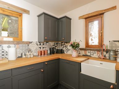 A kitchen with dark grey cabinets wooden countertops patterned tile backsplash a white sink and two wooden framed windows at Pentre Barn in Llantilio Pertholey near Mardy