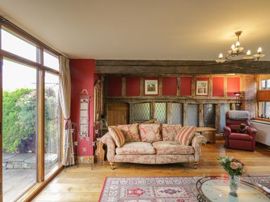 A living room with a floral sofa a red armchair a glass coffee table with flowers and large windows at Pentre Barn in Llantilio Pertholey near Mardy