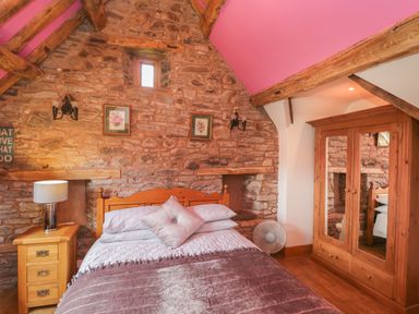 A bedroom with a wooden bed bedside table lamp fan and mirrored wardrobe at Pentre Barn in Llantilio Pertholey near Mardy