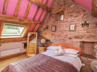 A bedroom with a wooden bed wooden side table lamp mirror and stone wall at Pentre Barn Llantilio Pertholey near Mardy