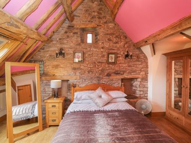 A bedroom with a wooden bed and bedside table under a stone wall and wooden beams at Pentre Barn in Llantilio Pertholey near Mardy