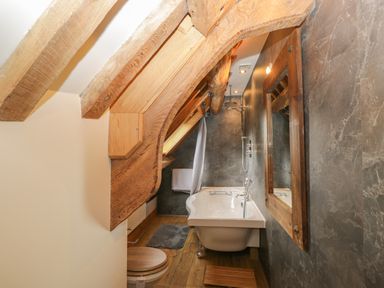A bathroom with wooden beams a bathtub a toilet a mirror and wooden floor at Pentre Barn in Llantilio Pertholey near Mardy