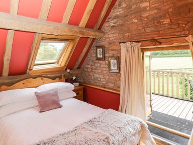 A bedroom with a bed and open door leading to a balcony at Pentre Barn in Llantilio Pertholey near Mardy