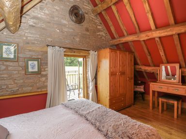 A bedroom with a wooden wardrobe dressing table bed and balcony door at Pentre Barn in Llantilio Pertholey near Mardy