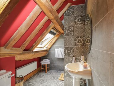 A bathroom with a pedestal sink a round mirror patterned tiles wooden beams and a skylight window at Pentre Barn in Llantilio Pertholey near Mardy