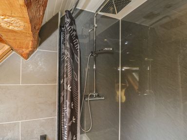 A shower area with a rainfall showerhead black patterned shower curtain and tiled walls at Pentre Barn in Llantilio Pertholey near Mardy