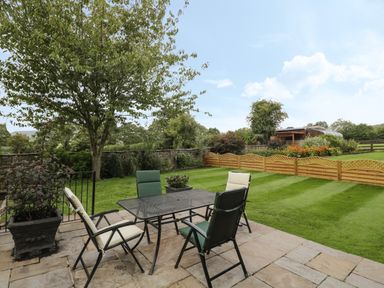 A garden patio with four chairs around a metal table and a lawn with plants and a wooden fence at Pentre Barn in Llantilio Pertholey near Mardy