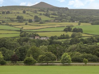 A landscape of rolling green hills with scattered trees and a few buildings at Pentre Barn in Llantilio Pertholey near Mardy
