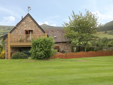 A stone house with a wooden balcony and garden with tree and shrubs at Pentre Barn in Llantilio Pertholey near Mardy