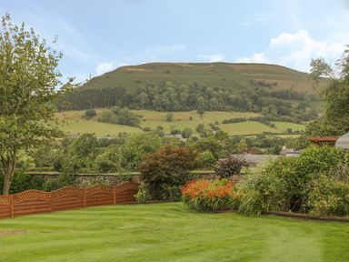 A garden with grass lawn trees flowers and shrubs with a hill in the background at Pentre Barn in Llantilio Pertholey near Mardy