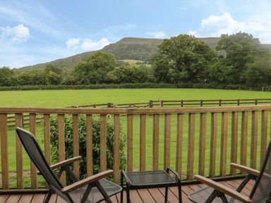 A balcony with two chairs and a small table overlooking a fenced grassy field and trees at Pentre Barn in Llantilio Pertholey near Mardy
