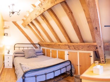 A bedroom with a metal bed frame wooden beams on the ceiling a bedside table and built in storage cupboards at Pentre Barn in Llantilio Pertholey near Mardy