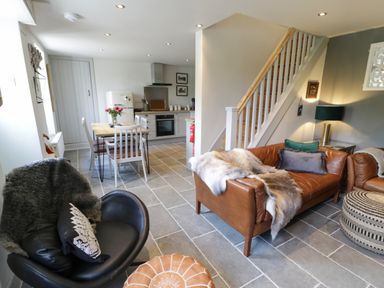 A living area with leather sofas and a black chair next to a dining table and kitchen at Swn yr Afon in Beddgelert