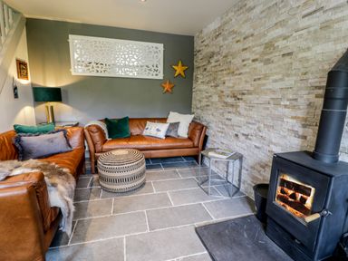 A living room with two leather sofas a round patterned ottoman a side table and a wood burning stove at Swn yr Afon in Beddgelert
