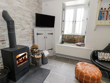 A room with a wood burning stove next to a television on a cabinet and a window seat with books at Swn yr Afon in Beddgelert