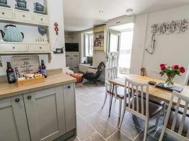 A dining area with a wooden table and chairs next to a doorway and a kitchen counter with cabinets at Swn yr Afon in Beddgelert