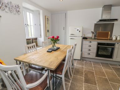 A kitchen with a wooden dining table and chairs a vase with flowers a refrigerator and an oven at Swn yr Afon in Beddgelert