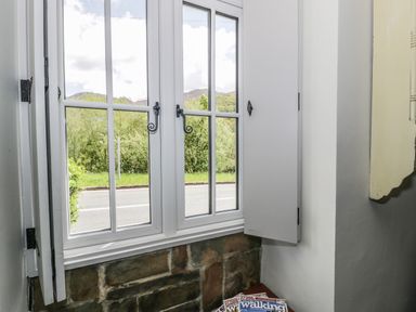 A window with shutters and magazines on a ledge inside at Swn yr Afon in Beddgelert
