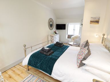 A bedroom with a metal bed frame towels on bed a chair a dresser a wall mirror and a window at Swn yr Afon in Beddgelert