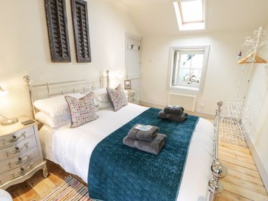 A bedroom with a made bed with folded towels on a teal runner and bedside tables with lamps at Swn yr Afon in Beddgelert