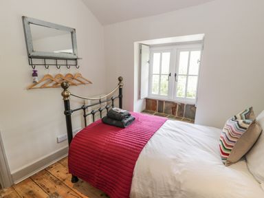 A bedroom with a bed, red blanket, gray towels, a window with stone sill, a mirror, and wooden floor at Swn yr Afon in Beddgelert