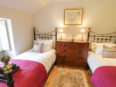 A bedroom with two single beds with red blankets a wooden chest of drawers with two lamps and a framed picture above at Swn yr Afon in Beddgelert
