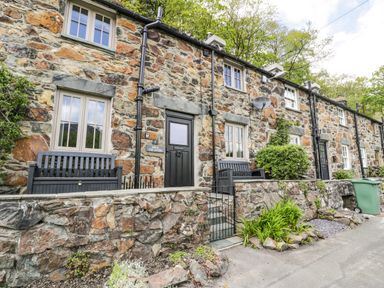 A row of stone cottages with black doors and windows and small garden beds at Swn yr Afon in Beddgelert