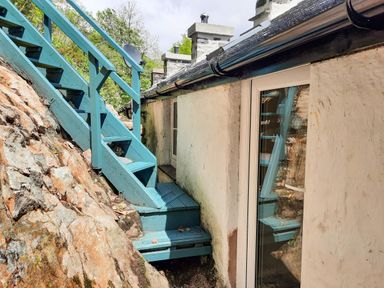 A blue wooden staircase next to a stone wall and a white building with windows at Swn yr Afon in Beddgelert