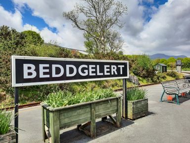 A train station platform with a Beddgelert sign wooden planters and a bench at Swn yr Afon in Beddgelert
