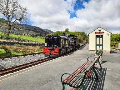 A steam train at a rural train station platform with a bench and small building in the foreground at Swn yr Afon in Beddgelert