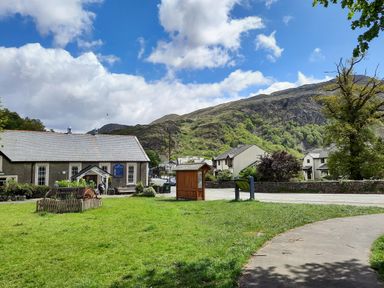A grassy park area with a path and wooden information boards near buildings and hills at Swn yr Afon in Beddgelert